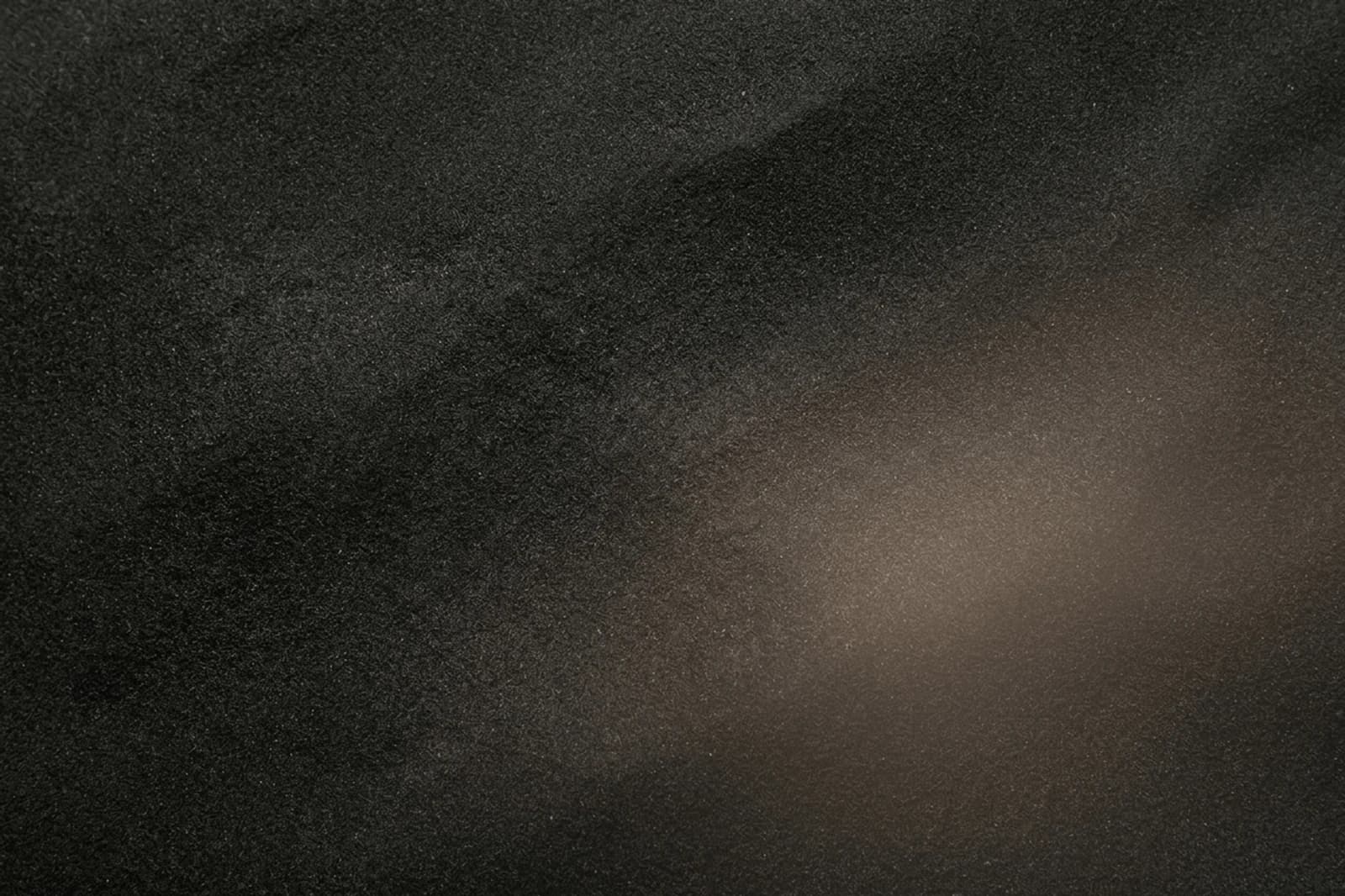 Dark satin abstract background with black sand texture, warm muted light, and premium calm