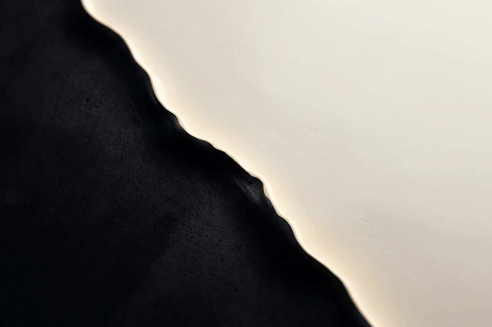 Premium abstract background with ivory and black material rift, warm edge light, and high-contrast depth